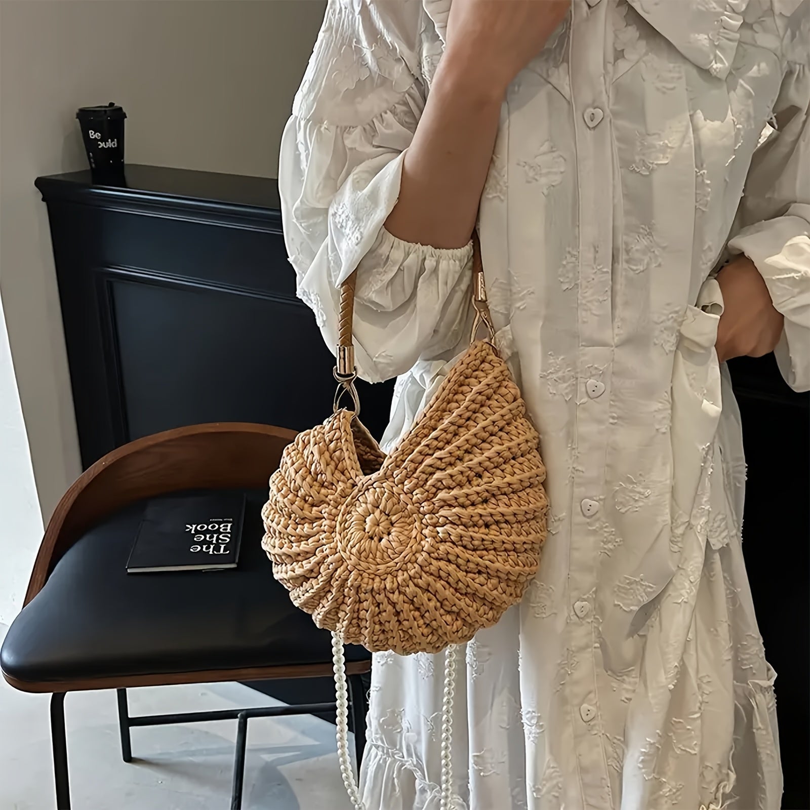 Modelo sosteniendo el bolso concha por el asa trenzada, con cadena de perlas