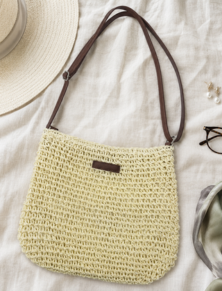 Bolso trenzado en tono crudo con correa marron ajustable, junto a un sombrero de paja y gafas