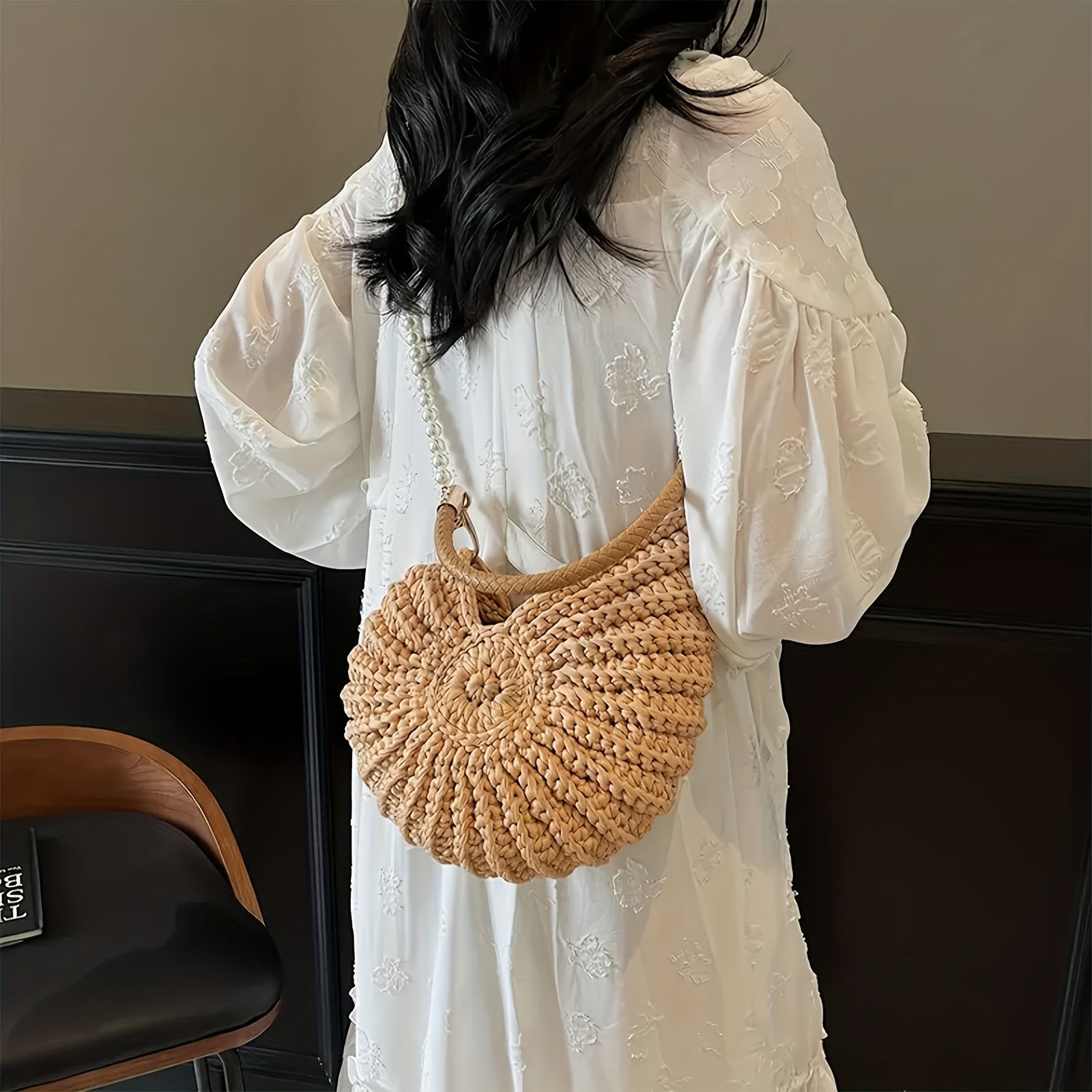 Modelo con vestido blanco llevando el bolso concha con cadena de perlas al hombro